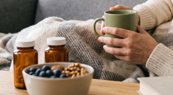 person holding a cup of tea next to supplement bottles